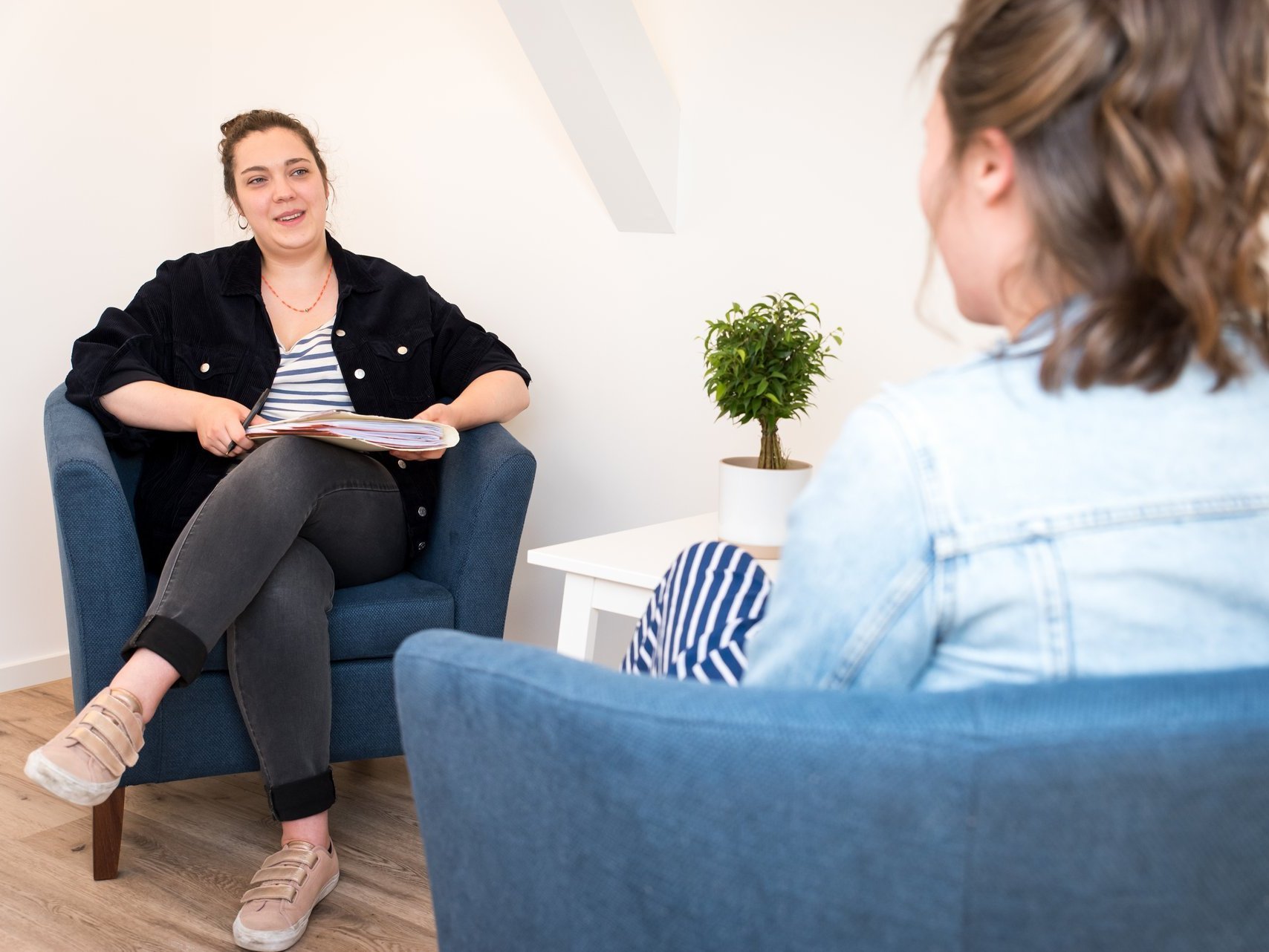 Zwei Frauen im Gespräch: sie sitzen an einem keinem Tisch in blauen Sesseln