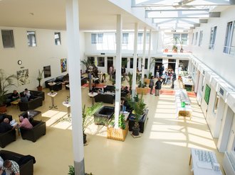 Überblick über den Aufenthaltsraum mit vielen Besuchern, die in Sofas und Sesseln sitzen oder an Stehtischen stehen