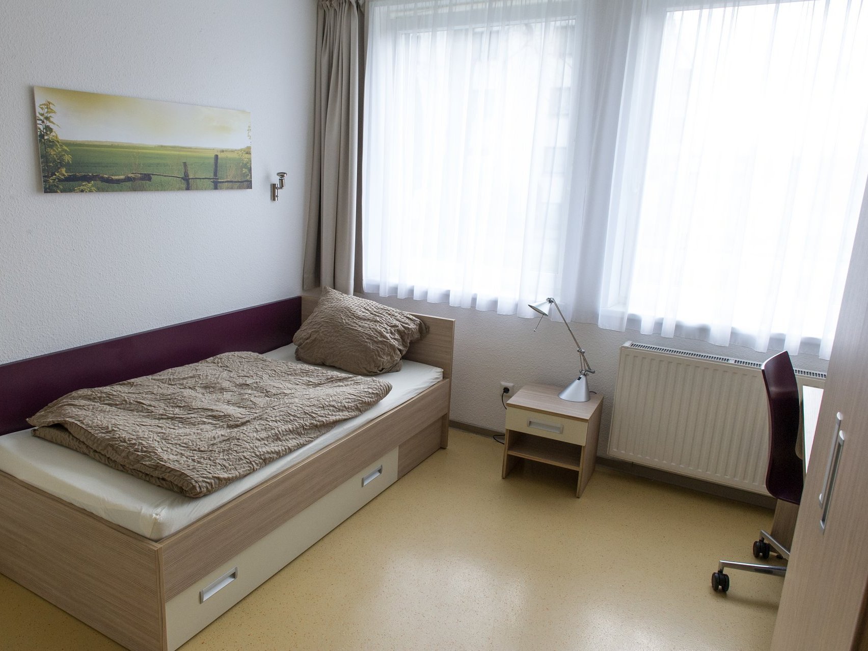 Ein Zimmer der Einrichtung: hell und funktionell mit Bett, Schreibtisch und Schrank