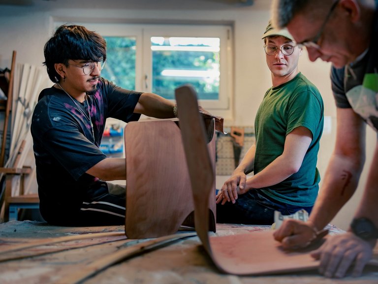 drei junge Maenner arbeiten in der Holzwerkstatt an Stuelen