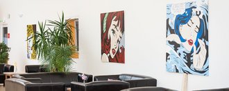 moderner Aufenthaltsraum: dunkle Ledersofas und -Sessel und Popart-Bildern