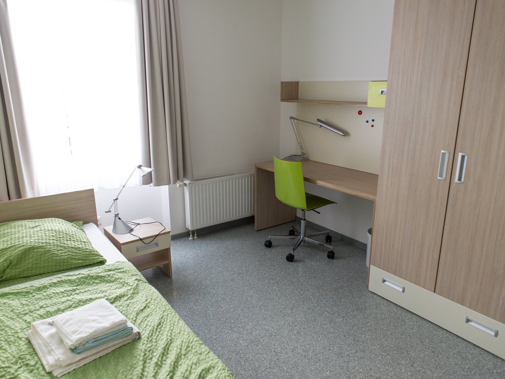 Ein Zimmer der Einrichtung: hell und funktionell mit Bett, Schreibtisch und Schrank