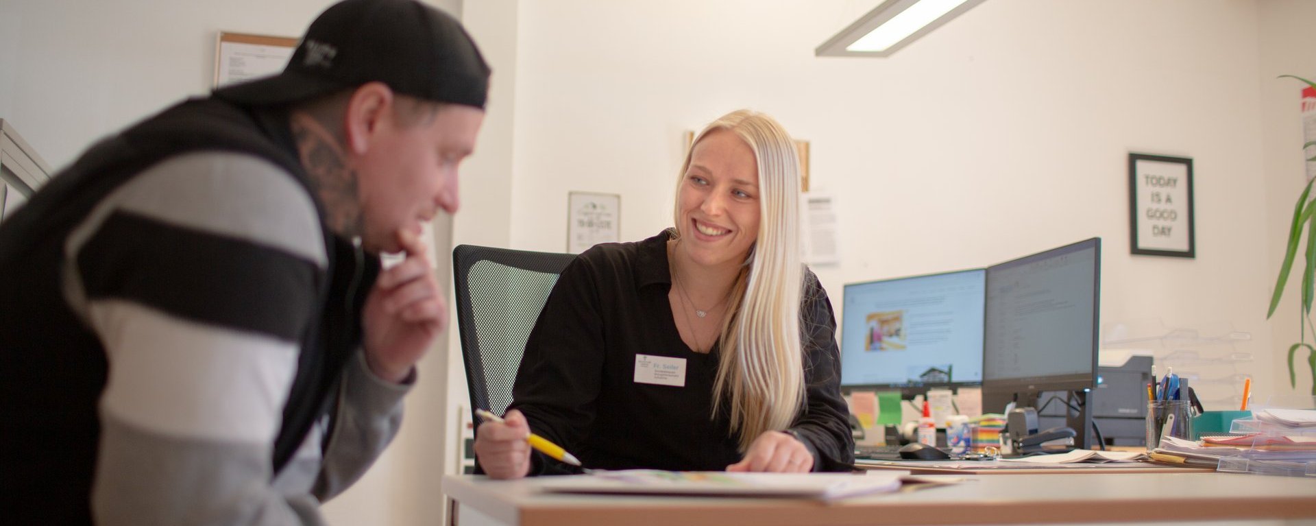 Eine freundliche Mitarbeiterin erklärt einem Besucher etwas anhand eines Schriftstücks